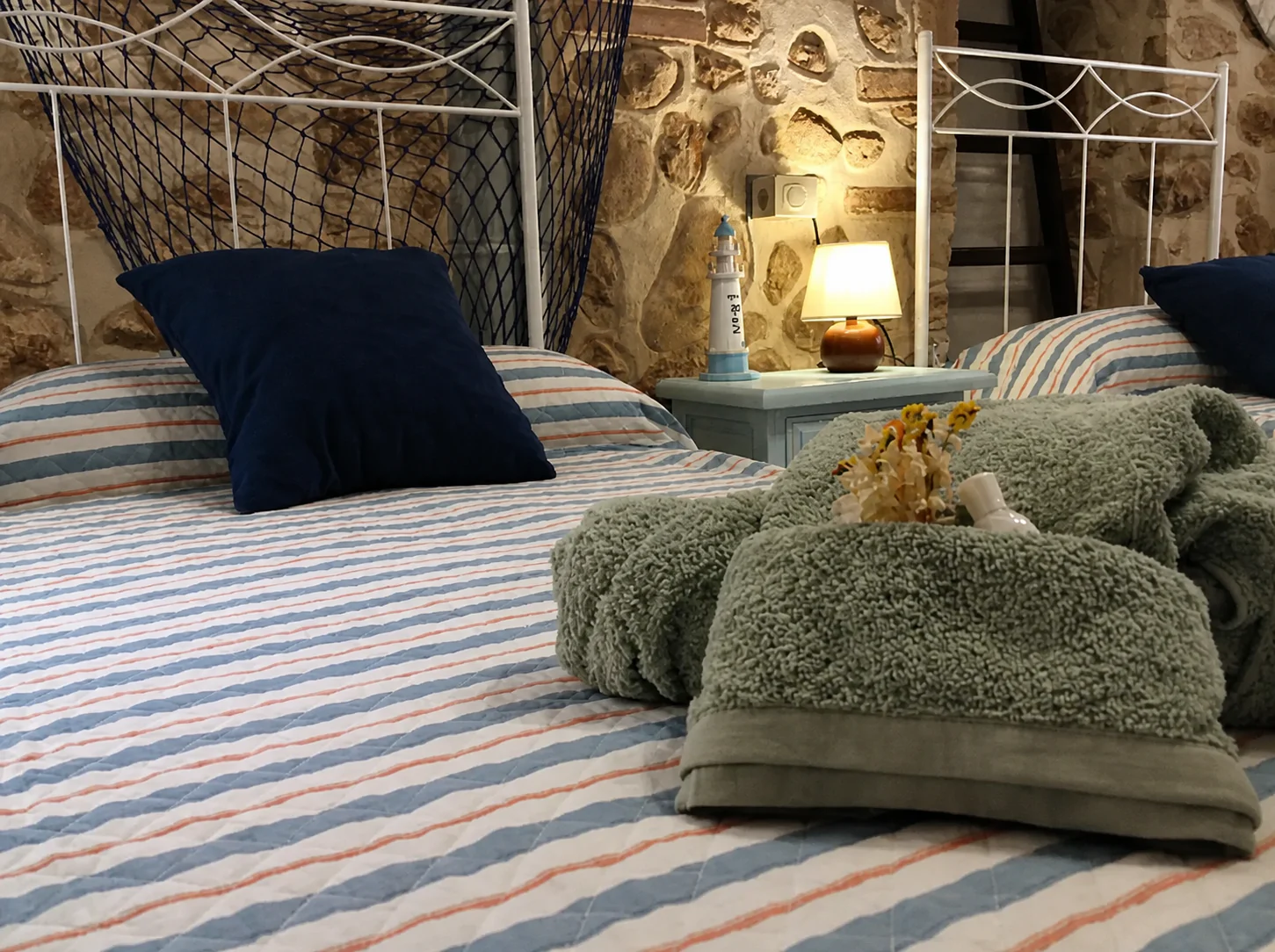 Camas individuales de la habitación Garbí con toallas dobladas y cojín azul marino.