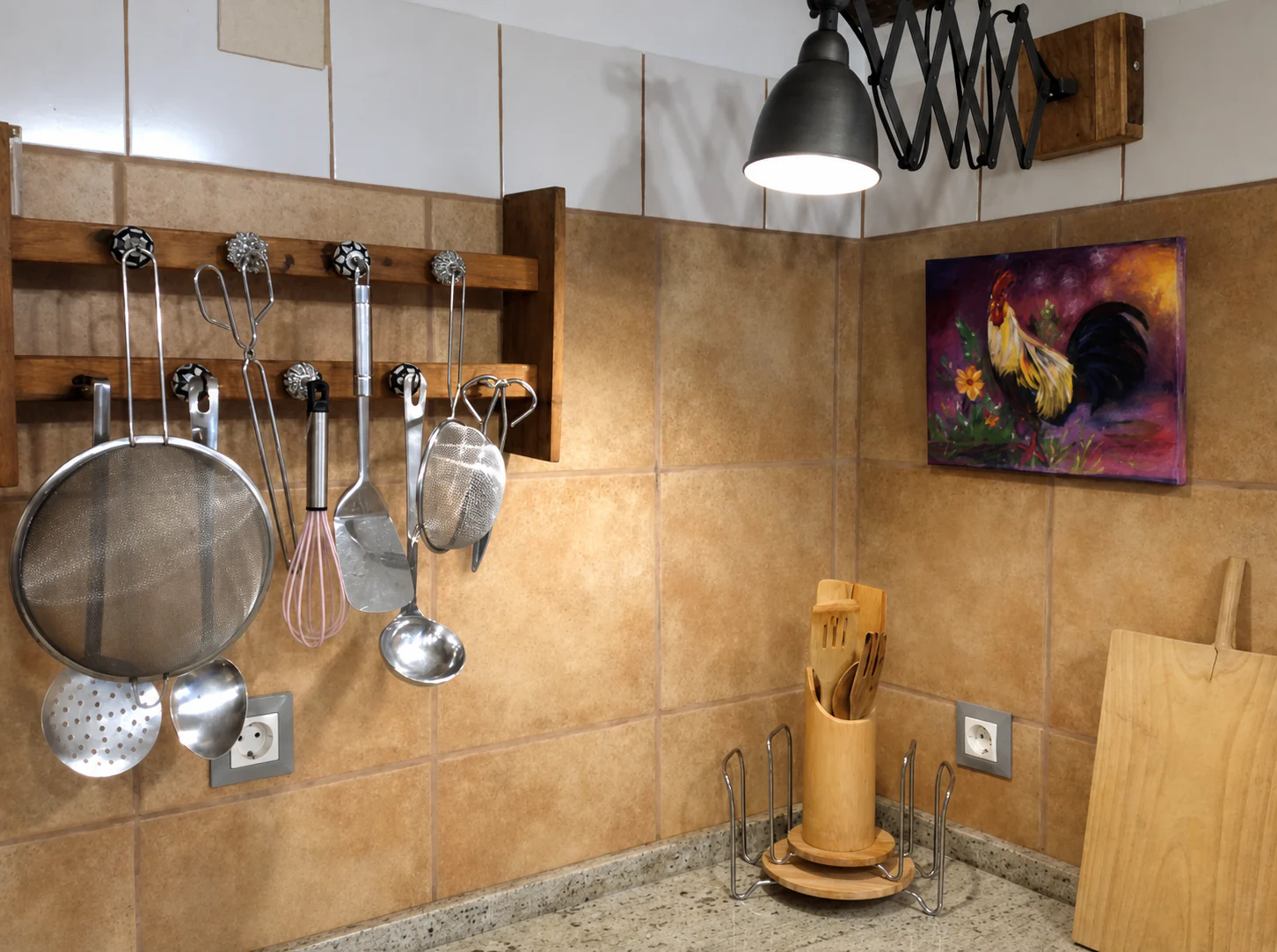 Utensilios de cocina colgados de una barra, lámpara de brazo extensible y un cuadro de un gallo.